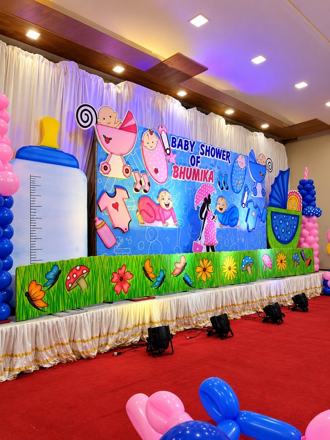 Baby shower stage with a custom illustrated backdrop, giant baby bottle cutout and balloon columns