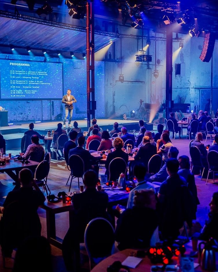 Speaker presenting on stage at a corporate conference with blue stage lighting